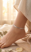 Close-up of a foot wearing a silver anklet with a soft, blurred background.